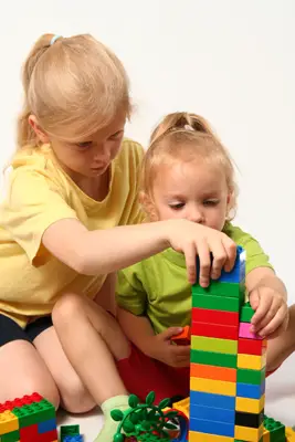 special needs child with sibling; young girls playing with blocks, legos