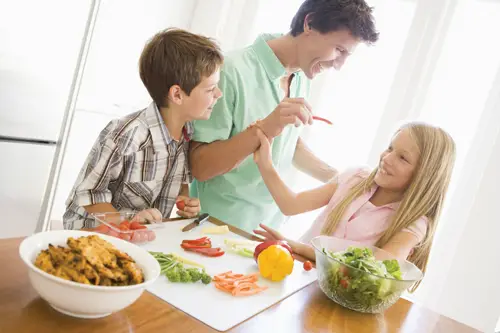 parents and kids in the kitchen; children eating vegetables, veggies; dad feeding daughter
