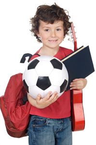 child juggling several activities; child holding soccer ball, guitar, and school books, backpack, bookbag