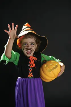 Little girl in scary halloween costume holding pumpkin; young girl dressed up as a witch for Halloween