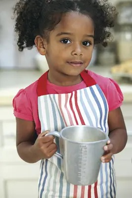 little girl baking, in the kitchen, wearing apron, holding measuring cup