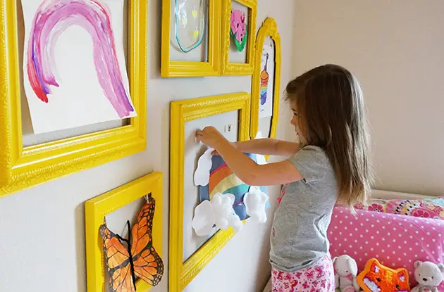 young girl hanging art in frames on wall