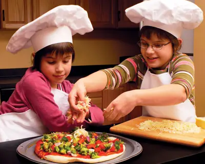 brother and sister making pizza, wearing chef hats